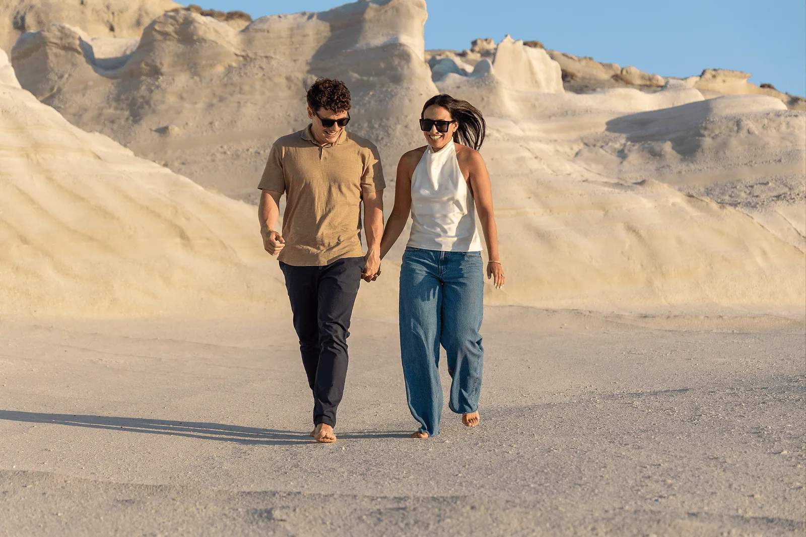 candid photo of happy couple walking on milos beach during sunset