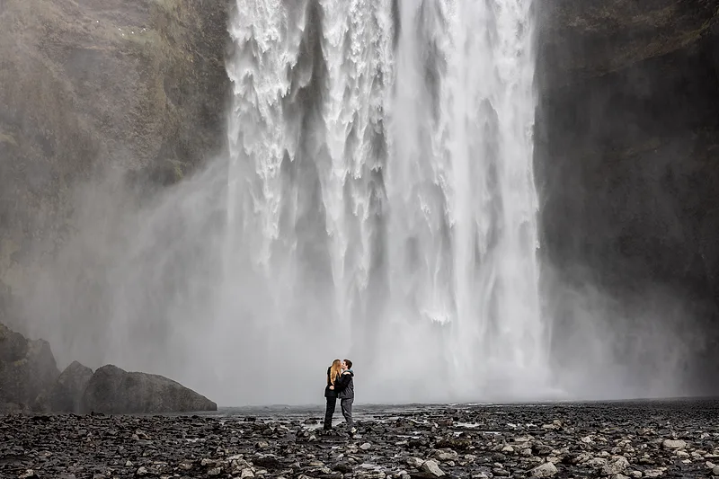 couple in iceland with a huge waterfall and rrainbow