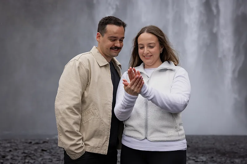 happy couple after proposal in iceland, woman looking at her new engagement ring