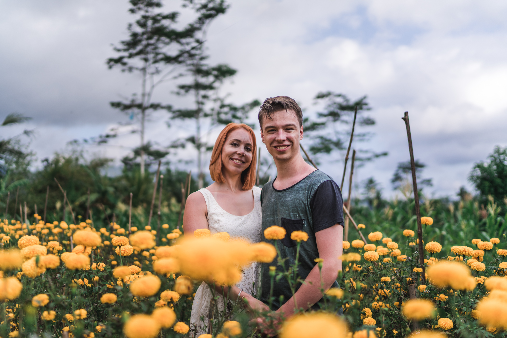 honeymoon photoshoot in bali: woman wearing white dress holding her new husband in the flowe field with yellow flowers