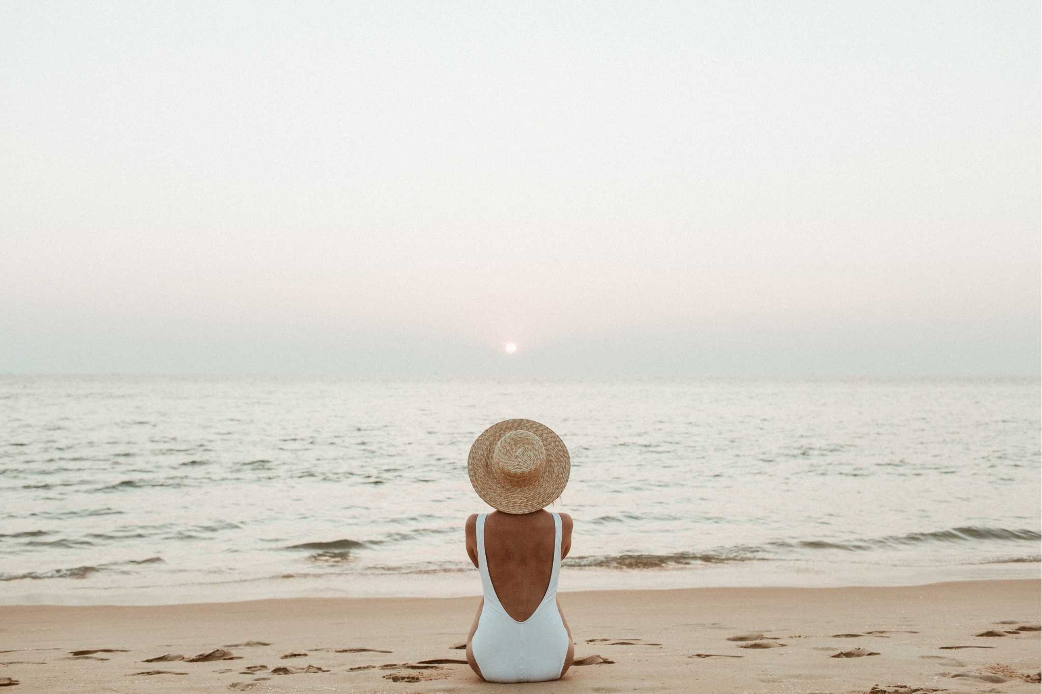 Woman in white swimsuit and straw hat on a beach